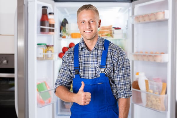 An appliance technician giving a thumb up in front of an open side by side refrigerator